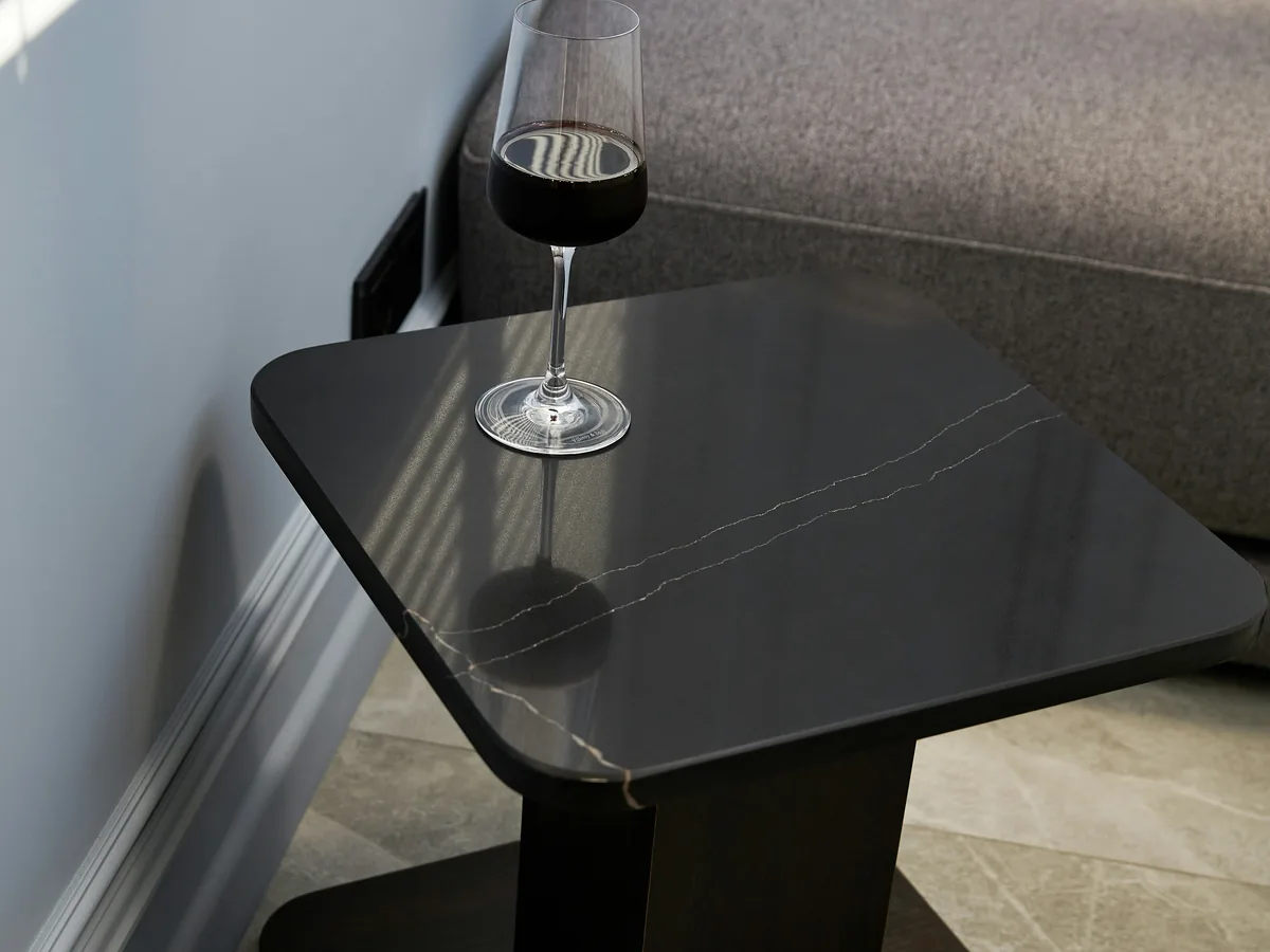 Table d'appoint noire avec un verre placée près d'un canapé gris