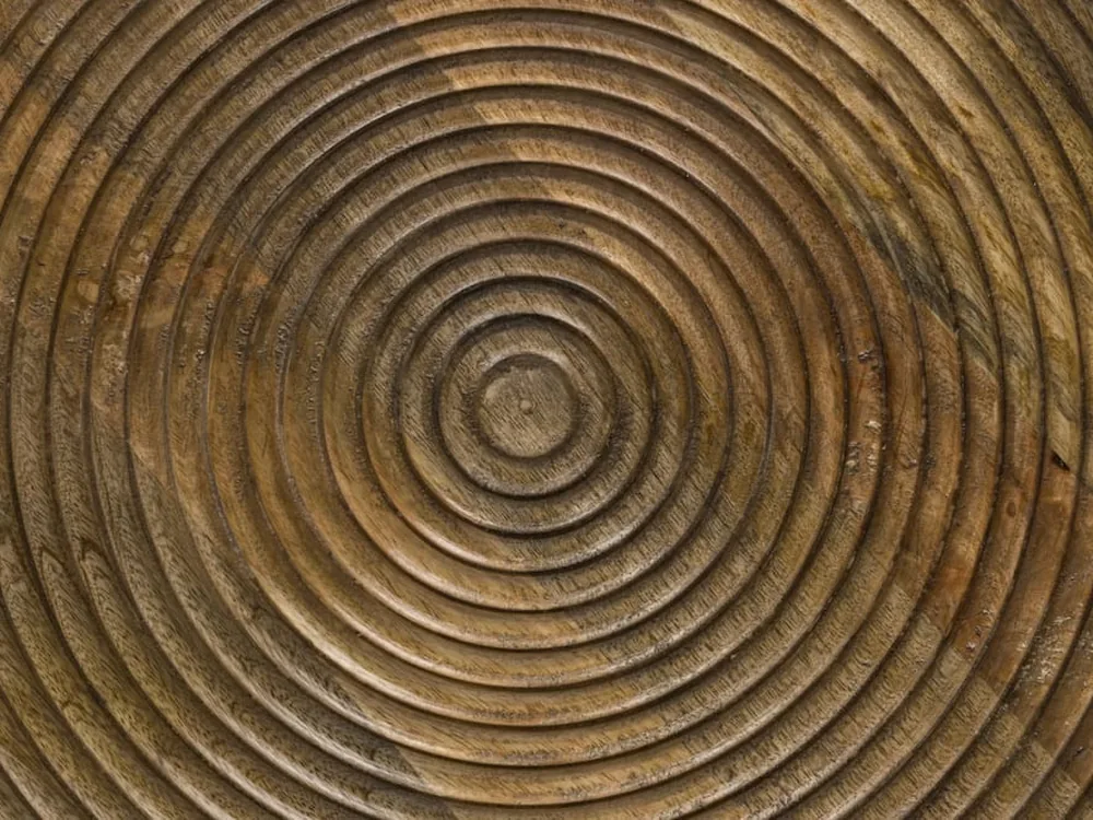 Gros plan sur le plateau en bois de manguier creusé de cercles concentriques, montrant le relief taillé et le fil du bois