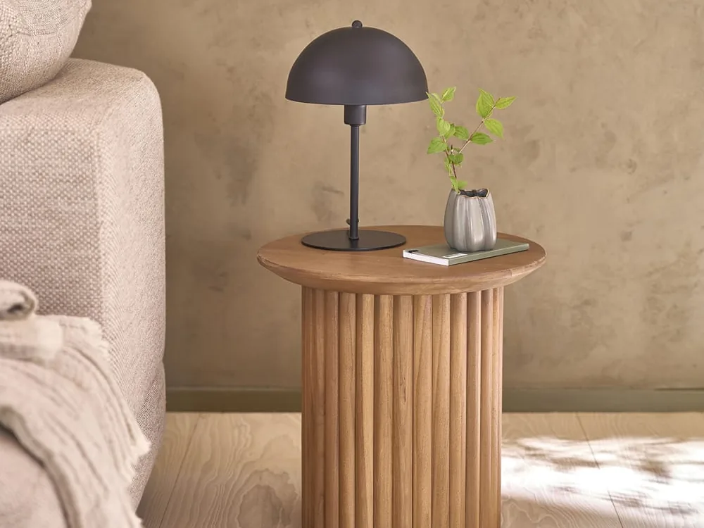 Bout de canapé rond en teck massif à fût cannelé, une lampe et un livre posés dessus, au pied d'un canapé beige
